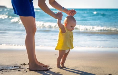 Mother helping her baby walk on a sandy beach