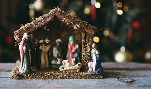 Nativity scene figurines with a Christmas tree in the background