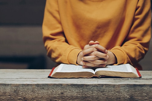Cropped shot of a woman's hands folded in prayer over a Bible