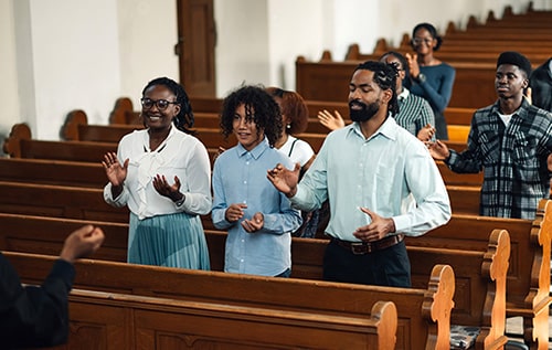 Congregation standing and praying with arms raised in church, focus on a Christian adoptive family in the front 