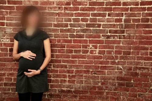 Pregnant woman standing in front of brick wall, face concealed