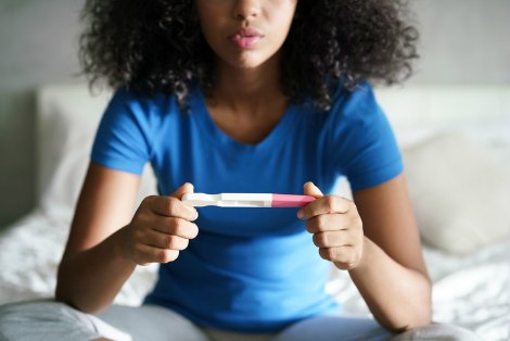 Woman sitting on bed and looking at pregnancy test