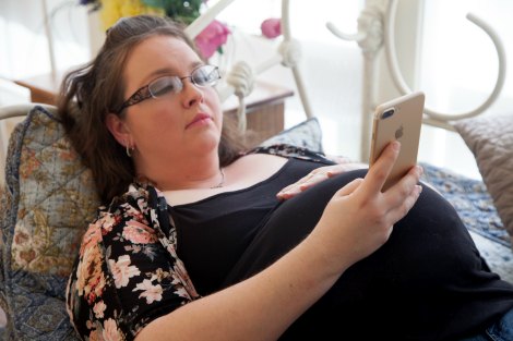 Pregnant woman lying on her bed, looking at Christian adoptive parents on her phone