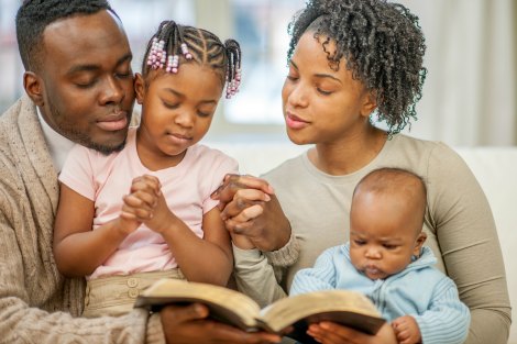 A family of four sitting on the couch together and are reading a Bible story.