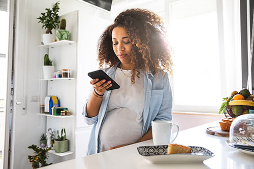 Pregnant woman in her kitchen, Googling how does the adoption process work on her phone
