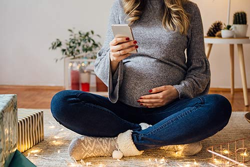 Young pregnant woman looks at her phone while thinking about adoption