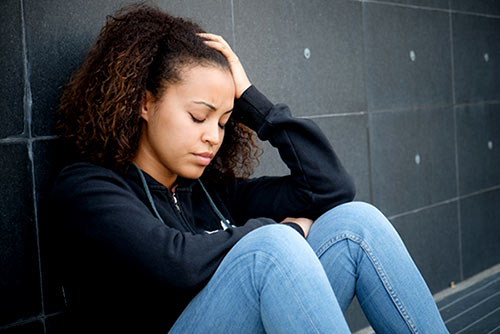 Young biracial woman sitting on the ground, in distress