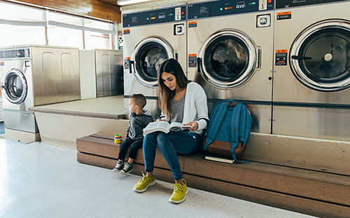 A struggling young mother does her homework while at the laundromat with her son